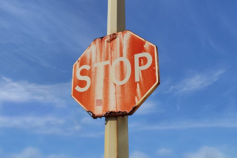 Old, rusty, faded Stop sign against blue sky with white wispy cl